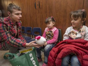 Noah Anderson, 17, a Grade 12 student at Holy Names high school, hands out a bag of donations to Tiresa Karmo, 7, and Miryam Karmo, 4, centre, newcomers from Iraq at the Multicultural Council of Windsor and Essex County on Dec. 9, 2016.