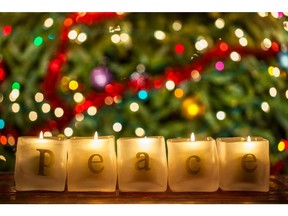 Burning candles spell the word 'peace' in front of a lit decorated Christmas tree.