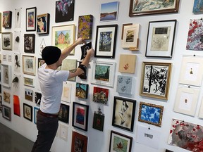 Joshua Babcock covers a wall full of local art in preparation for Doin' the Louvre, Artcite's 35th annual Christmas fundraiser at the gallery in Windsor on Dec. 7, 2016.