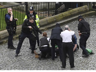 A policeman points a gun at a man on the floor as emergency services attend the scene outside the Palace of Westminster, London, March 22, 2017.