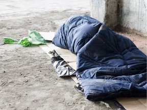 A homeless man sleeps in sleeping bag on cardboard.