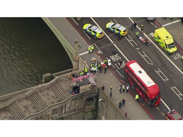 In this image taken from video  emergency personnel gather around a body on the southside of Westminster Bridge that leads to the Houses of Parliament in London, March 23, 2017 after the House of Commons sitting was suspended as witnesses reported sounds like gunfire outside.