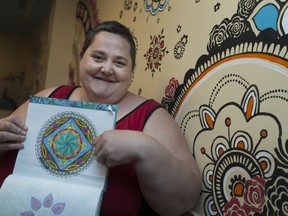 Erika Edwards, a resident at Victoria Manor, stands against a cafeteria wall adorned with mandalas on June 15, 2017, showing off the mandala she coloured.