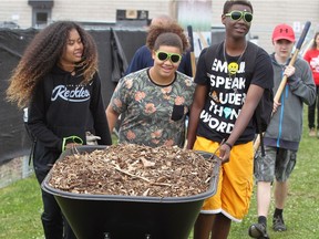 Walkerville students Mikayla Whitfield, left, Janai Beck and Rapheal Amegashie carry a wheelbarrow of mulch during United Way Centraide's ChangeTheWorld program in the community garden located at Unemployed Help Centre on Cantelon Drive Monday June 5, 2017.