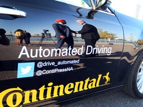Navdeep Bains, federal minister of innovation, science, and economic development, shakes hands with Ontario transportation minister Steven Del Duca, as reflected on the side of a Continental Automated Driving vehicle in Windsor on July 31, 2017.