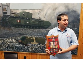 Curator Kevin Fox at Kingsville Historical Park museum Aug.10, 2017. In photo, Fox holds medals from Essex Scottish Regiment in front of painting depicting Canadian Army on the bloody beaches.