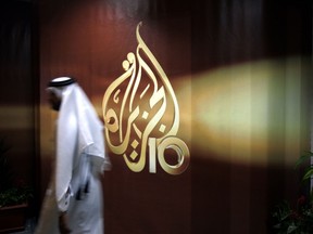 In this file photo, a Qatari employee of Al Jazeera Arabic language TV news channel walks past the logo of Al Jazeera in Doha.