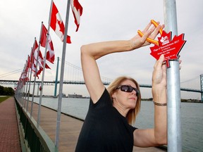 Terri Davis-Fitzpatrick of Veterans Voices of Canada on Tuesday removes a maple leaf plaque dedicated to a fallen soldier at the Flags of Remembrance display at Assumption Park. The plaques, which honour Canadian armed forces heroes, have been disappearing since last Saturday's unveiling ceremony.