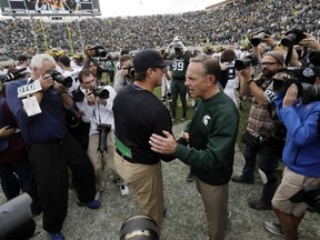 In this Oct. 29, 2016, photo, Michigan head coach Jim Harbaugh, left, greets Michigan State head coach Mark Dantonio after the Wolverines won 32-23 in an NCAA college football game in East Lansing, Mich. It's the biggest week of the year for Michigan State and Michigan. This year, the game comes early in the conference season, and it'll be under the lights in Ann Arbor.