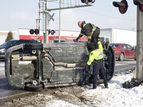 A tow truck operator gets a helping hand from a Windsor police officer at the scene of a single-vehicle rollover on Tecumseh Road East on Feb. 8, 2018. The driver of the Kia Rio escaped with minor injuries.