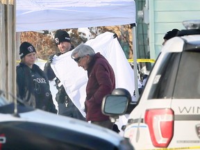 Coroner Dr. Robert Drake, right, views evidence while a Windsor Police officer holds a white sheet where the body of a man was found on Feb. 14, 2018.  Windsor Police arrived after an area resident found the body while heading to work in the early morning.