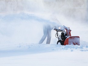 A man with a snow blowing machine clears a sidewalk.