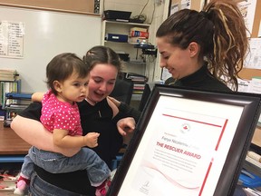 Fenyx Aubin-LeBlanc (centre) shows her Red Cross Rescuer Award to her 10-month-old cousin Nora, who Fenyx saved from choking in January 2018. Nora's mother, Nicolette LeBlanc, looks on. Photographed at Saint-Antoine French Catholic elementary school on March 27, 2018.