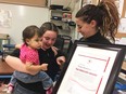 Fenyx Aubin-LeBlanc (centre) shows her Red Cross Rescuer Award to her 10-month-old cousin Nora, who Fenyx saved from choking in January 2018. Nora's mother, Nicolette LeBlanc, looks on. Photographed at Saint-Antoine French Catholic elementary school on March 27, 2018.