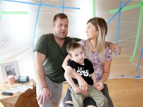 Ryan and Cadi White and their son, Lawson, 3, sit on Monday, April 2, 2018, in front of a protective barrier after dangerous mould was found beneath the walls during the construction of a lift for Lawson.