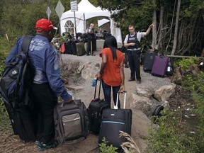 In this Aug. 7, 2017 file photo, a Royal Canadian Mounted Police officer informs a migrant couple of the location of a legal border station, shortly before they illegally crossed from Champlain, N.Y., to Saint-Bernard-de-Lacolle, Quebec. (AP Photo/Charles Krupa, File)