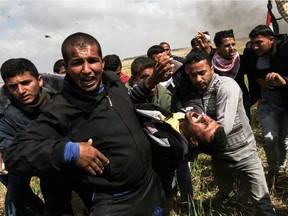 An injured Palestinian man is carried by fellow protesters as they run for cover during clashes with Israeli security forces following a demonstration commemorating Land Day near the border with Israel, east of Khan Yunis, in the southern Gaza Strip on March 30, 2018.