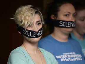 Amanda Thomashow, 28, left, and Alex Neil-Sevier, 29, wear silence gags while listening to the Michigan State University board meeting on April 13, 2018, in Lansing, Mich. Interim Michigan State University President John Engler said Friday that he regrets the school's response to a woman filing a federal rape lawsuit against the university.