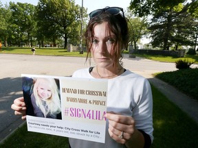 On the corner of Prince Road and Barrymore Street, Courtney Belanger holds information for a petition after her niece, Lila Jane Zuest, 4, was struck by a bus on Prince Road Saturday.