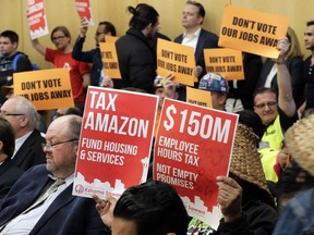 FILE - In this May 9, 2018, file photo, opponents and supporters of a controversial proposal to tax large businesses such as Amazon.com to fund efforts to combat homelessness hold signs as they attend a Seattle City Council committee meeting at City Hall in Seattle. A divided Seattle City Council is set to decide Monday, May 14, 2018, on the proposal to tax large businesses to fight homelessness.