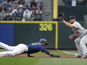 Seattle Mariners' Jean Segura (2) dives safely back to first base on a pickoff attempt as Detroit Tigers first baseman John Hicks reaches for the throw during the first inning of a baseball game Friday, May 18, 2018, in Seattle.