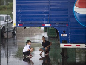 WINDSOR, ONT:. JUNE 23, 2018 -- Stevie Valaris, 8, and Anthony Beloulis, 10, take cover from the rain under a Pepsi truck at the Greek Village on the last weekend of the Carrousel of Nations, Saturday, June 23,  2018.