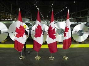 A member of the A/V team straightens Canadian flags in front of rolls of coated steel at Stelco in Hamilton before a visit by Chrystia Freeland, Minister of Foreign Affairs, on June 29, 2018. Canada announced $16.6-billion worth of retaliatory tariffs that took effect July 1 on dozens of U.S. products, from strawberry jam to screws and nails, making good on threats of a tariff war after the U.S. implemented levies on Canada's steel and aluminum.