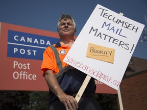 Posties walk. Phil Lyons, president of CUPW Local 630, holds a picket sign in front of the Canada Post office in Tecumseh on July 16, 2018. Mail carriers held an information picket.