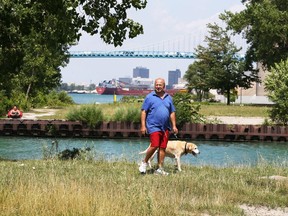 Terry Potomski and his dog Hailey walk on Aug. 2, 2018, through a well-groomed riverfront lot at Russell and Mill streets the city is seeking to expropriate from its Michigan owner.