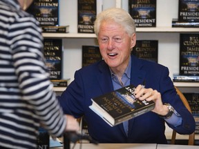 In a June 28, 2018, file photo, former U.S. president Bill Clinton holds a copy of "The President is Missing" at Book Revue, in Huntington, NY. The book, co-written with James Patterson, has more than 1 million sales in North America.