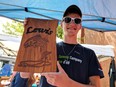 Jordyn Lewis holds one of the wood signs he made with his homemade CNC cutting machine to sell at the Small Business Centre tent during Buskerville Festival in Walkerville on Aug. 12, 2018. Lewis is one of 19 student entrepreneurs participating in the Summer Company Program.