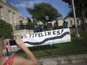 Protestors opposed to Kinder Morgan's proposed replacement pipe under the Detroit River attach a  banner to the fence outside Mackenzie Hall during a public meeting there on Aug. 28, 2018 .