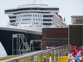 A woman relaxes on a patio near the docked luxury liner Queen Mary 2 in the Halifax Harbour on June 13, 2017.