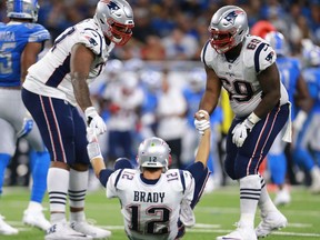 Trent Brown #77 of the New England Patriots and Shaq Mason #69 help their quarterback Tom Brady #12 up off the field after a sack during the second half at Ford Field on Sept. 23, 2018 in Detroit.