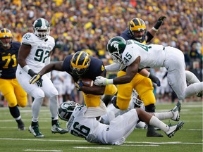 Running back De'Veon Smith of the Michigan Wolverines is tackled by cornerback Arjen Colquhoun and linebacker Darien Harris of the Michigan State Spartans during the second quarter of the college football game at Michigan Stadium on Oct. 17, 2015 in Ann Arbor, Michigan.