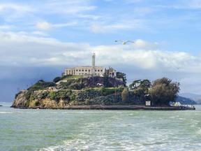 The Alcatraz Penitentiary, now a museum, in San Francisco, California, United States of America. A view of the island, the lighthouse, prison buildings and the San Francisco Bay from the coast on a sunny day.