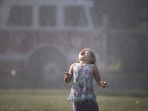 Eastlynd Manners, 3, lets the water fall onto her tongue as water falls from the ladder of a Windsor Fire and Rescue truck during the service's second week of Hot Summer Nights at Gary Dugal Park in Ford City, Thursday, July 28, 2018.