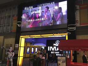 In this Tuesday, Dec. 4, 2018, photo, a worker stands underneath a screen advertising the movie "Crazy Rich Asians" at a cinema in Beijing. Chinese audiences aren't exactly going nuts over the U.S. box office hit "Crazy Rich Asians," despite its all-Asian cast and theme of rising Asian prosperity.