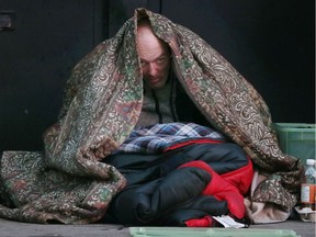 John Rollo glances through an opening in his blanket while sitting on the cold Ouellette Avenue sidewalk collecting donations.