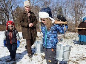 Myles Keith, 7, carries maple syrup pails strung to a yoke while his brother Bryce Keith, 4, left, waits his turn on the first day of maple syrup season at John R. Park Homestead. Homestead staffers Duncan Wright and Kyrsten Burns, right, were dressed in 1850's attire and they guided visitors to several stages of maple sap collection and processing. The Maple Syrup Festival runs at John R. Park Homestead March 2-3, 2019.