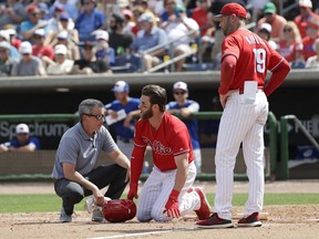 Philadelphia Phillies' Bryce Harper, center, yells toward Toronto Blue Jays pitcher Trent Thornton as manager Gabe Kapler, right, and assistant trainer Chris Mudd check on him after he was hit by a pitch during the sixth inning in a spring training baseball game, Friday, March 15, 2019, in Clearwater, Fla. Harper sustained a bruised right foot Friday, but manager Gabe Kapler said the team wasn't overly worries about the injury. Initial X-rays were negative, the team said, but Harper then left the ballpark for more detailed X-rays.