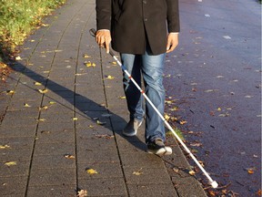 A blind person walks on the street using a red and white walking stick, also known as a white cane. Getty Images.