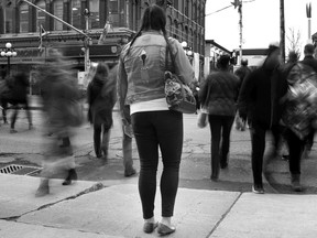 A woman stands on the sidewalk as people cross a street in this undated photo illustration. A national hotline to help victims and survivors of human trafficking is now taking calls, with the organization behind the initiative saying it hoped the service would also fill crucial gaps in public knowledge about the issue.
