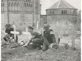 British and Canadian troops are being buried side by side with French civilians in a Normandy cemetery. The soldiers placing flowers on the graves are Pte. W. Yoing of Sydney, N.S., Pte. H. Roach of Ottawa, and Pte. M.G. Newberry of Victoria, B.C. (File photo)