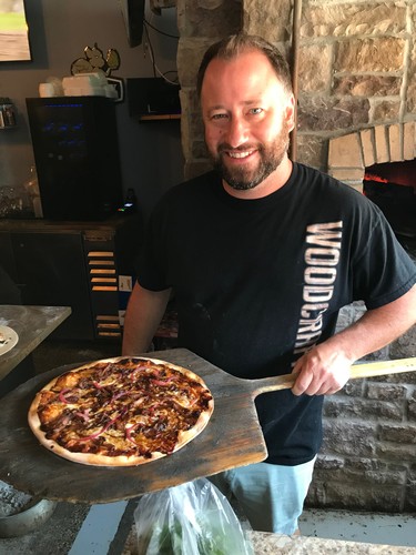 Ryan Casier, co-owner of Woodcraft Pizza and Bar in Essex, proudly displays his Korean Short Rib pizza, fresh from the oven.