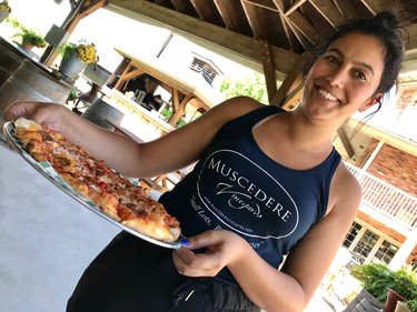 Melissa Muscedere of Muscedere Vineyards smiles as she delivers the signature Muscedere pizza, hot from the oven, complete with homemade tomato sauce, mozzarella, Italian sausage, banana peppers and a touch of onion.