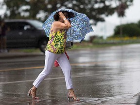 A woman shields herself from sudden rain while crossing Riverside Drive in downtown Windsor on July 2, 2019.