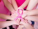 Women hold a pink ribbon, which symbolizes breast cancer prevention.
