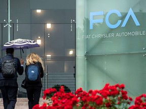 In this May 27, 2019, photo, people walk past the logo of Fiat Chrysler Automobiles (FCA) at the Fiat Mirafiori car plant in Turin, Italy.