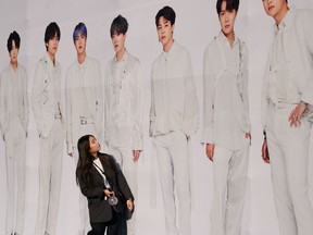 In this Oct. 29, 2019, photo, a fan of South Korea's BTS K-pop group poses against a backdrop featuring an image of the band members, as they arrive for the final concert of their world tour at the Olympic stadium in Seoul. The BTS world tour which began in August 2018 and ended on Oct. 29 drew a total audience of more than two million at 62 shows in 23 cities, according to Big Hit Entertainment.